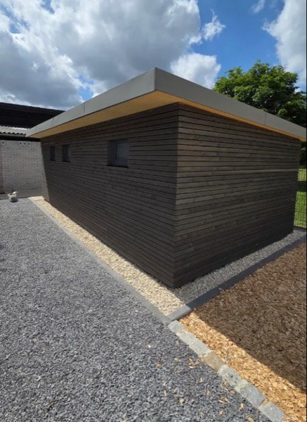 Anbau mit dunkler Holzfassade aus schmalen Leisten und umlaufender Flachdachattika.