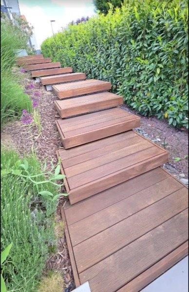 Gartenweg aus einzelnen, freischwebend wirkenden Holz-Trittstufen entlang einer Hecke.