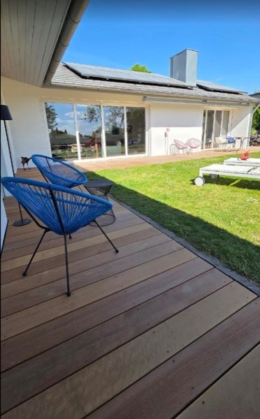 Neu gebaute Holzterrasse aus dunklen Dielen mit Rasenfläche und Sitzmöbeln.